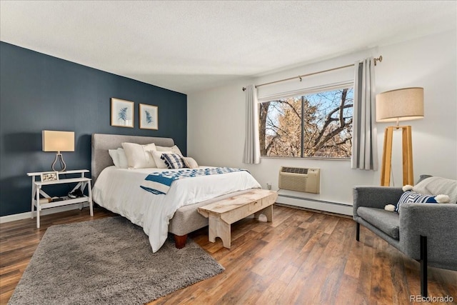 bedroom featuring an AC wall unit, wood finished floors, baseboard heating, and a textured ceiling