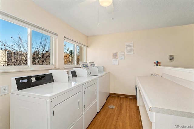 community laundry room featuring baseboards, light wood finished floors, washing machine and clothes dryer, ceiling fan, and a textured ceiling