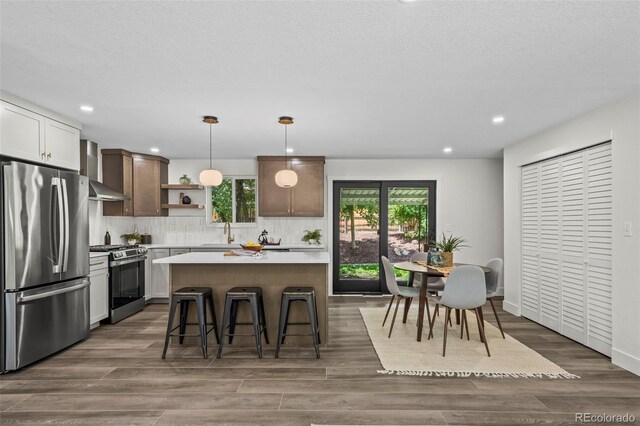 10067 W 68th Pl, Arvada, CO 80004 - kitchen with stainless steel appliances, wall chimney range hood, open shelves, light countertops, and decorative backsplash