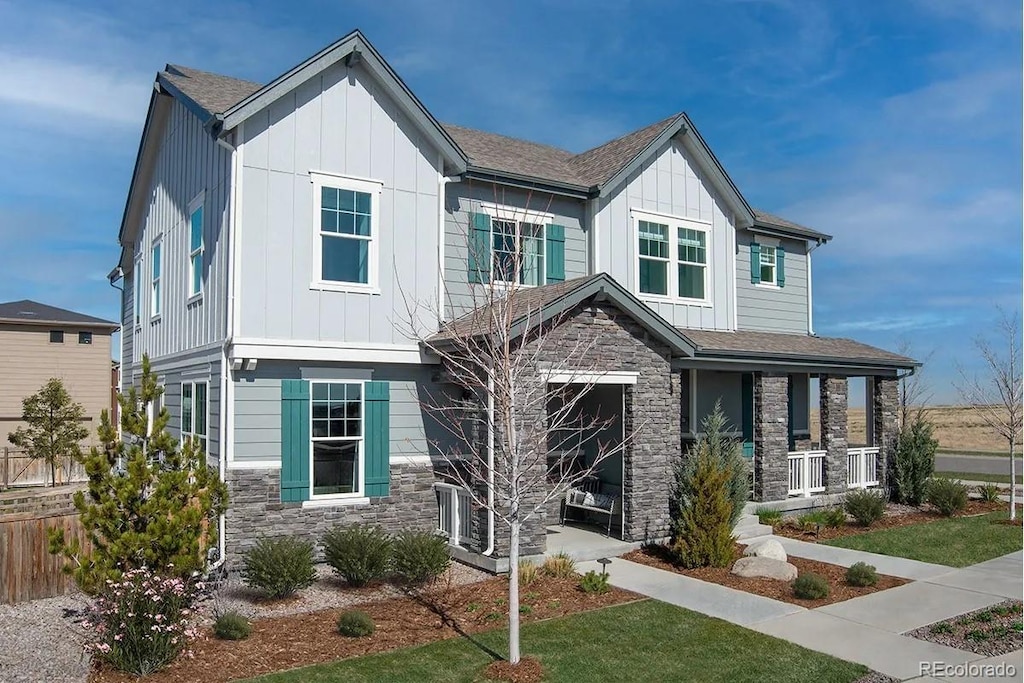 view of front of property with stone siding, a porch, board and batten siding, and a front yard