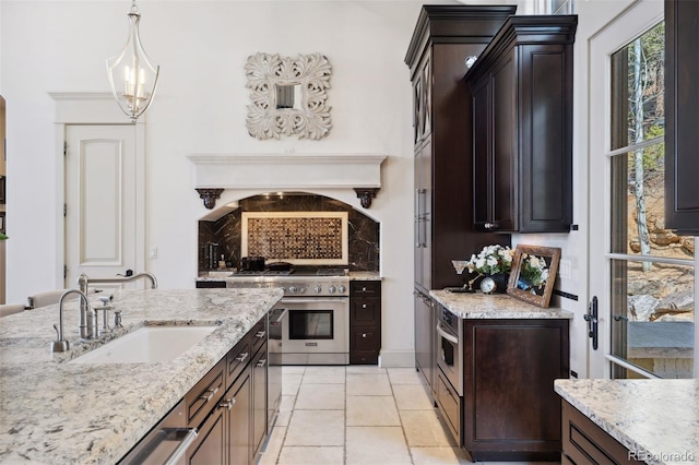 kitchen featuring dark brown cabinetry, light stone counters, appliances with stainless steel finishes, pendant lighting, and a sink