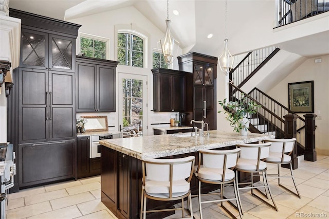 kitchen featuring hanging light fixtures, a kitchen island with sink, wall oven, high vaulted ceiling, and a breakfast bar area