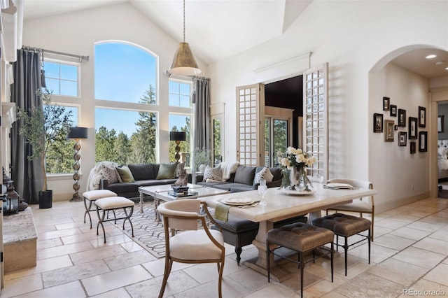 dining room featuring high vaulted ceiling, arched walkways, stone tile floors, and baseboards