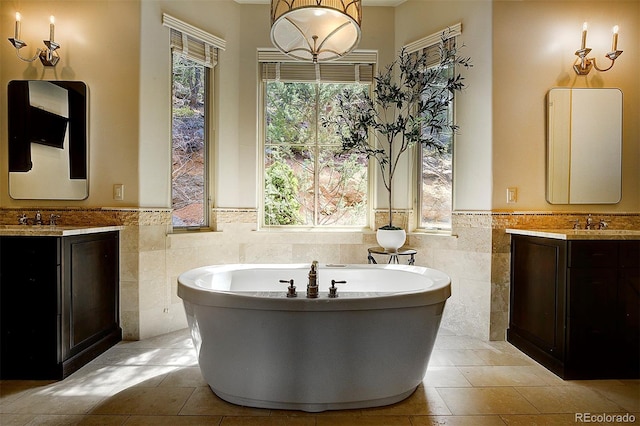 full bathroom with a freestanding bath, a sink, tile walls, wainscoting, and two vanities