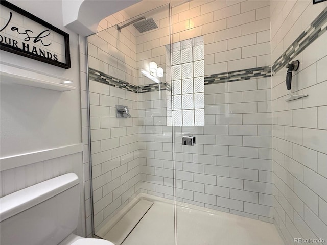 full bath featuring toilet, tiled shower, and a wainscoted wall