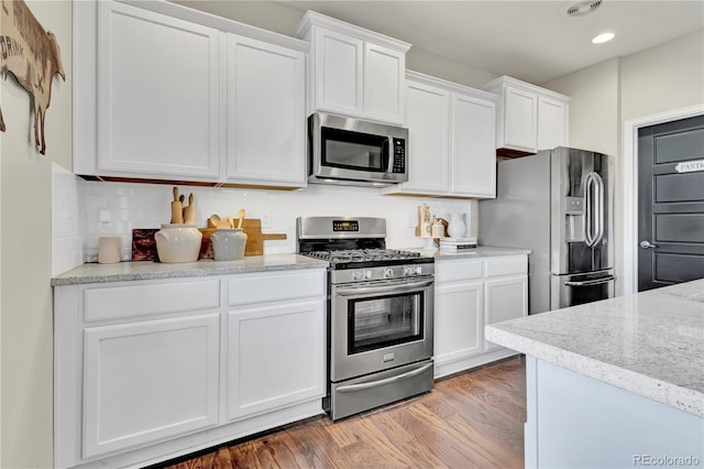 kitchen with white cabinetry, appliances with stainless steel finishes, backsplash, and light hardwood / wood-style floors