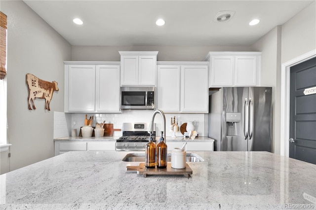 kitchen with light stone countertops, white cabinetry, appliances with stainless steel finishes, and decorative backsplash