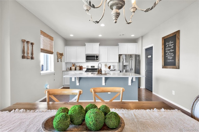 kitchen featuring stainless steel appliances, a kitchen island with sink, white cabinets, and an inviting chandelier