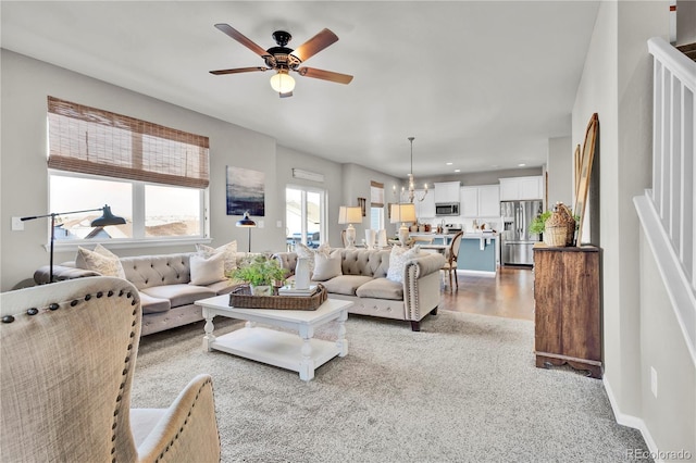 living room with ceiling fan with notable chandelier and light carpet