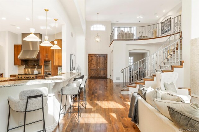 155 S Poplar St, Denver, CO 80230 - kitchen featuring brown cabinets, wall chimney exhaust hood, hardwood / wood-style floors, light stone counters, and backsplash