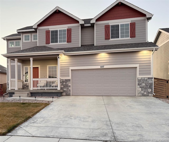 craftsman inspired home with an attached garage, covered porch, a shingled roof, concrete driveway, and stone siding