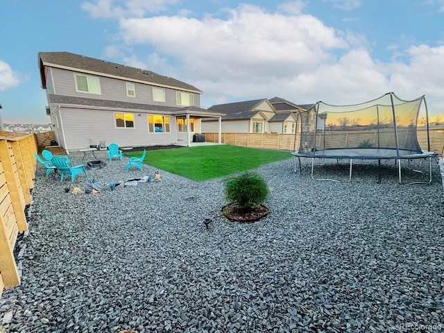 back of property with a trampoline, a fenced backyard, and a lawn