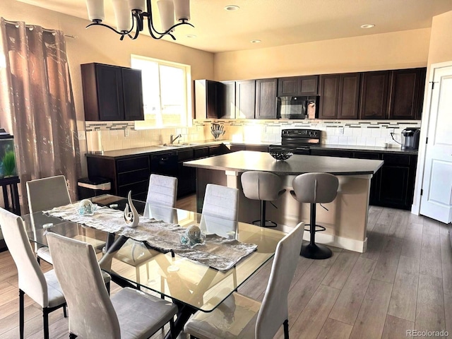 kitchen with a sink, black appliances, tasteful backsplash, and light wood-type flooring