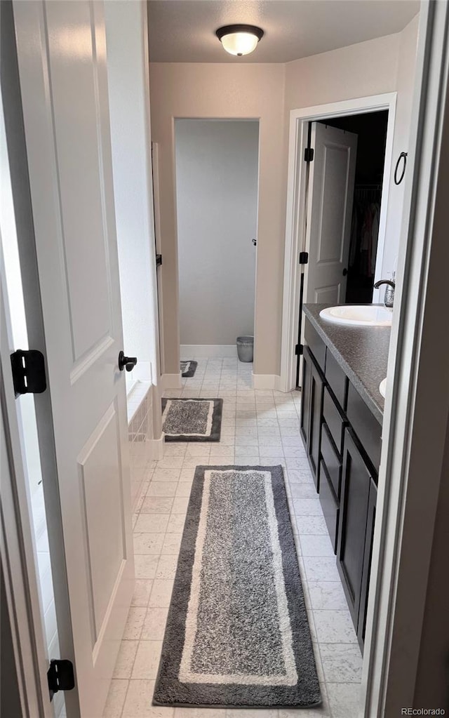 bathroom featuring baseboards, double vanity, a sink, a walk in closet, and tile patterned floors