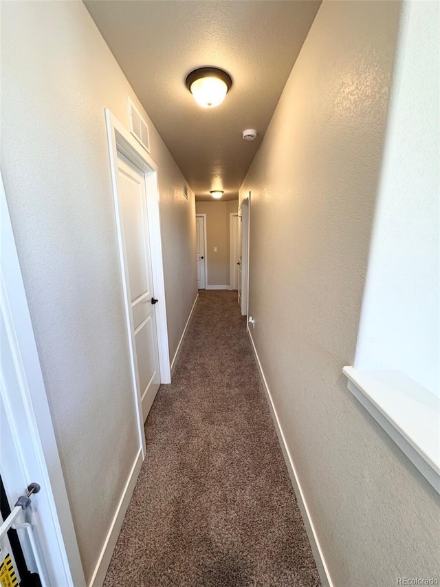 hall featuring baseboards, visible vents, a textured ceiling, and carpet