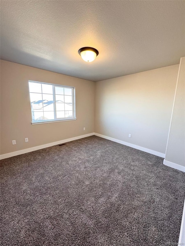 spare room with baseboards, visible vents, dark carpet, and a textured ceiling