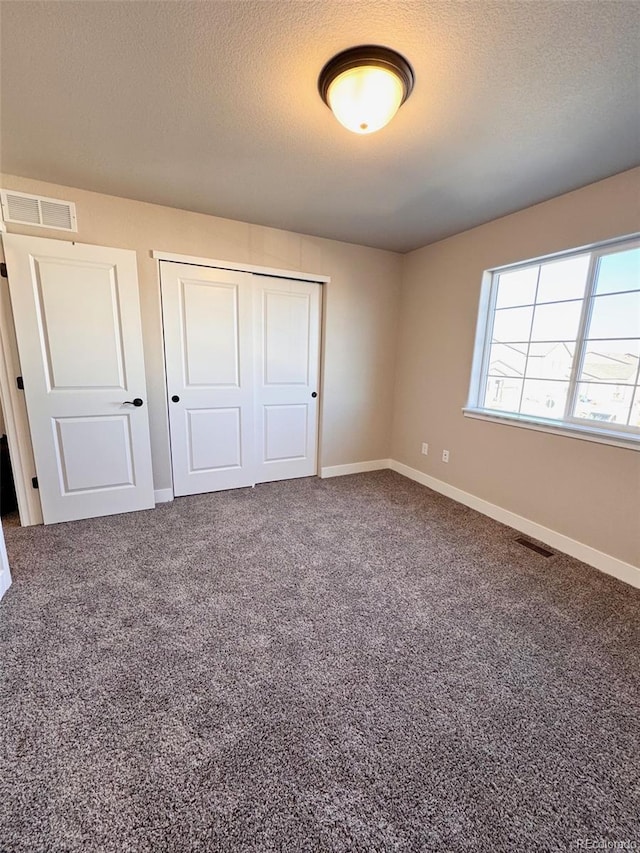 unfurnished bedroom with a closet, visible vents, a textured ceiling, and carpet