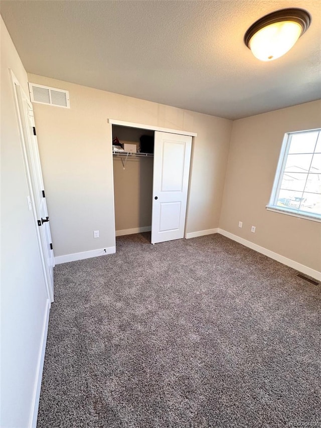 unfurnished bedroom featuring visible vents, carpet floors, a textured ceiling, and a closet