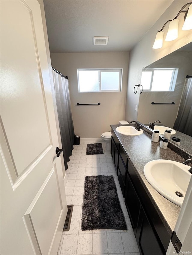 bathroom with double vanity, visible vents, toilet, and a sink