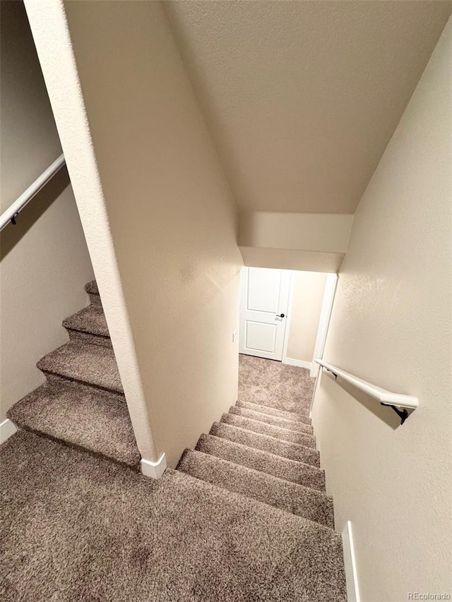 staircase featuring lofted ceiling, carpet flooring, a textured wall, and a textured ceiling