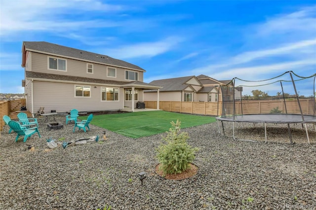 rear view of property featuring a lawn, a fire pit, a fenced backyard, and a trampoline