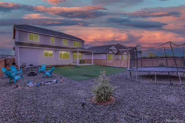 back of house featuring a fire pit, a patio, a fenced backyard, a trampoline, and a yard