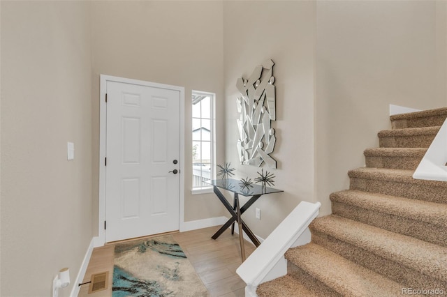foyer entrance featuring a towering ceiling, visible vents, stairway, baseboards, and light wood-style flooring