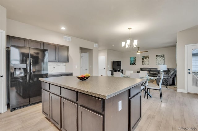 kitchen with backsplash, a kitchen island, light wood-type flooring, a notable chandelier, and black fridge