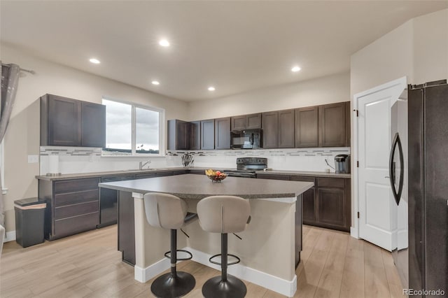 kitchen featuring decorative backsplash, dark brown cabinetry, a kitchen island, black appliances, and light wood finished floors
