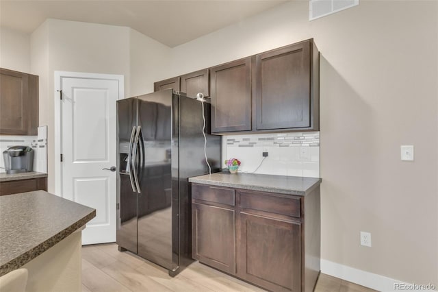 kitchen with dark brown cabinetry, dark countertops, black fridge, tasteful backsplash, and visible vents
