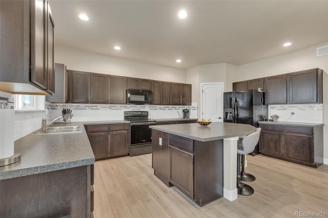 kitchen with decorative backsplash, a kitchen breakfast bar, a center island, a sink, and black appliances