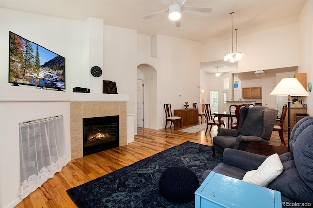 living room featuring ceiling fan with notable chandelier, a high ceiling, a tile fireplace, and light hardwood / wood-style floors