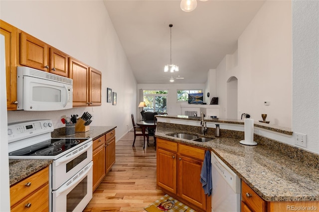 kitchen with white appliances, light hardwood / wood-style floors, high vaulted ceiling, dark stone counters, and sink