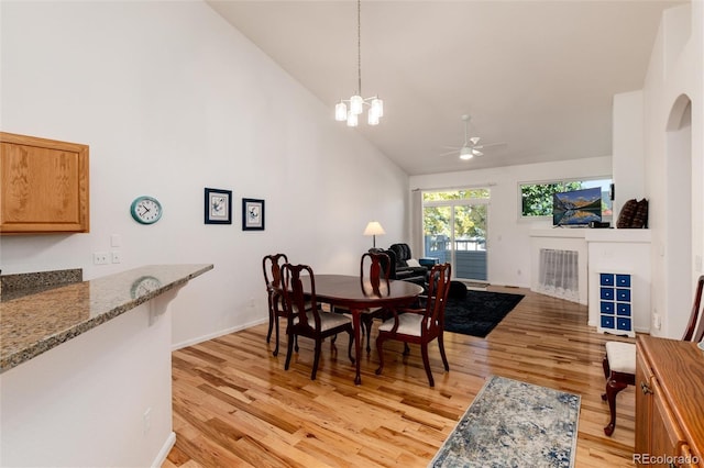 dining space featuring ceiling fan with notable chandelier, high vaulted ceiling, and light wood-type flooring