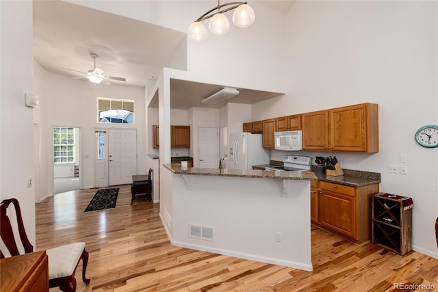 kitchen featuring white appliances, decorative light fixtures, a towering ceiling, dark stone counters, and a kitchen breakfast bar