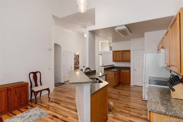 kitchen featuring light hardwood / wood-style floors, ceiling fan, dark stone counters, a kitchen bar, and sink