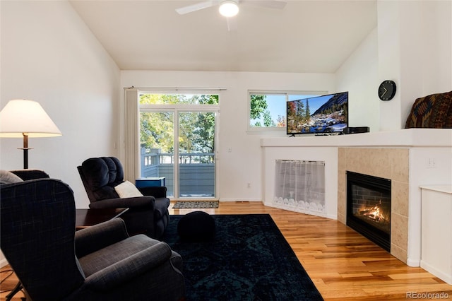 living room featuring ceiling fan, a tile fireplace, hardwood / wood-style floors, and vaulted ceiling