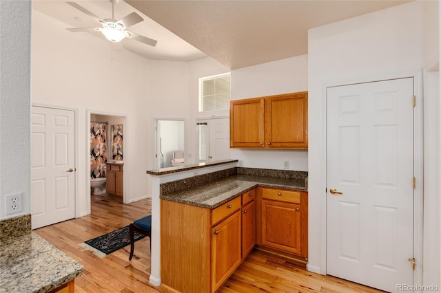 kitchen featuring ceiling fan, light hardwood / wood-style flooring, kitchen peninsula, dark stone counters, and a high ceiling