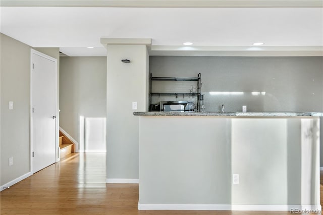 bar with light stone countertops and light hardwood / wood-style flooring