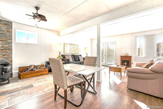 dining area with beam ceiling, a warm lit fireplace, a wood stove, and wood finished floors