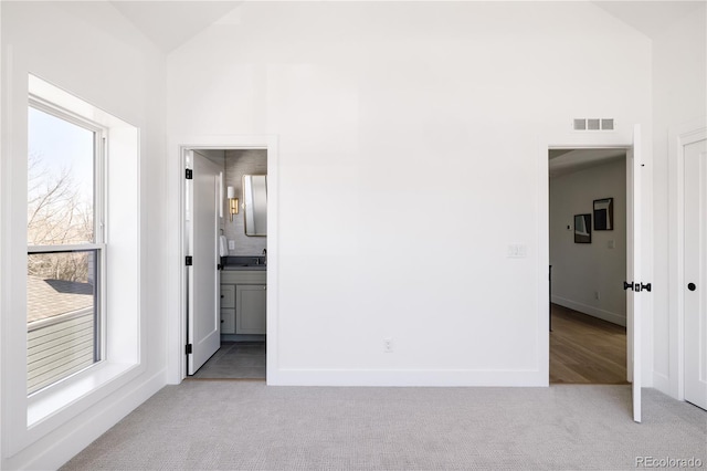 unfurnished bedroom featuring vaulted ceiling, light carpet, ensuite bathroom, and multiple windows