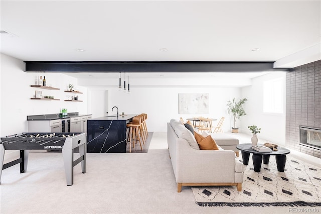 living room featuring beamed ceiling, a tile fireplace, beverage cooler, sink, and carpet