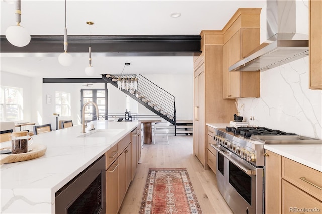 kitchen featuring stainless steel appliances, wall chimney range hood, a sink, light brown cabinets, and light wood-type flooring