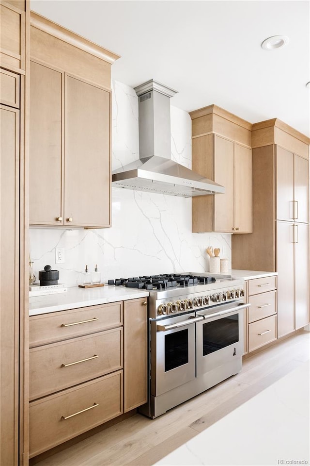 kitchen with wall chimney exhaust hood, double oven range, light brown cabinets, and light countertops