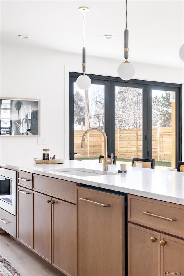 kitchen featuring a sink, built in microwave, light wood-type flooring, and pendant lighting