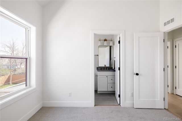 unfurnished bedroom featuring light carpet, a sink, baseboards, and ensuite bath