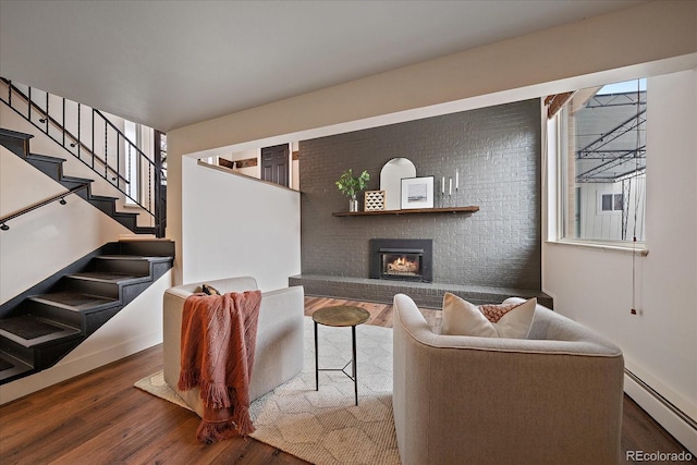 living room with baseboard heating, dark hardwood / wood-style floors, brick wall, and a fireplace