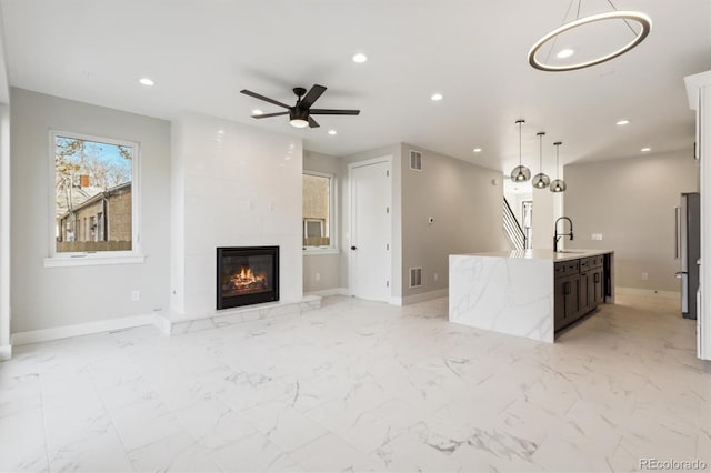 unfurnished living room with a fireplace, ceiling fan, and sink