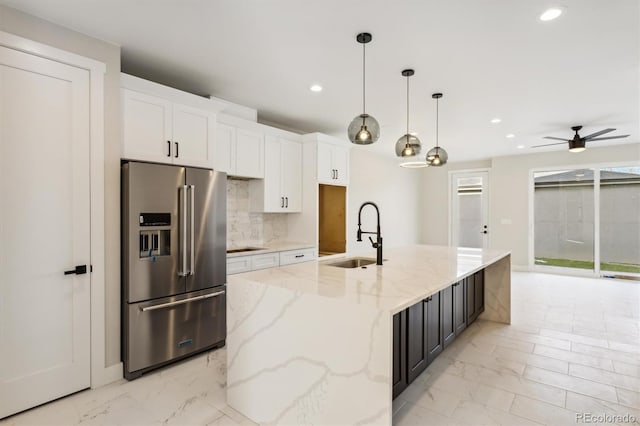 kitchen with sink, light stone countertops, an island with sink, high end fridge, and white cabinetry