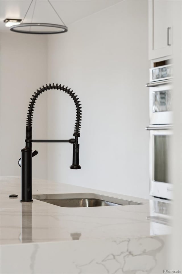 interior details featuring white cabinets, light stone countertops, sink, and double oven